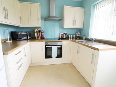 A kitchen with cream cabinets wooden countertops microwave oven sink and blue walls at Anneddle in Four Mile Bridge