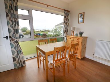 A dining area with a wooden table and four chairs next to a large window with patterned curtains at Anneddle in Four Mile Bridge