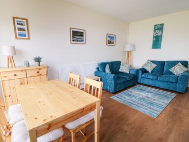 A dining area with wooden table and chairs next to a living space with blue sofas and a rug at Anneddle in Four Mile Bridge