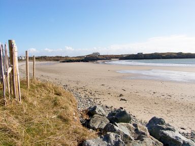 A sandy beach with rocks and grass beside a wooden fence at Anneddle in Four Mile Bridge