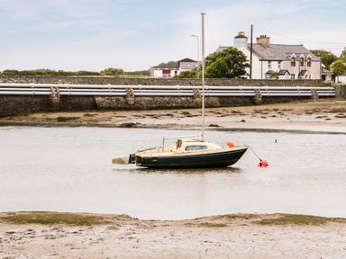 A sailboat anchored in shallow water near a shore with a house and pipes in the background at Anneddle in Four Mile Bridge