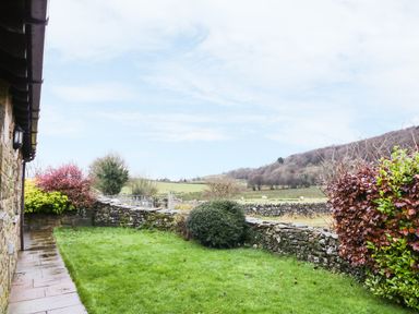 A stone house with a grassy garden and stone walls with hills in the background at Hill Bank in Hutton Roof