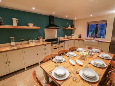 A kitchen with a wooden dining table set with white dishes and glasses and cabinets along teal and cream walls at Hill Bank in Hutton Roof