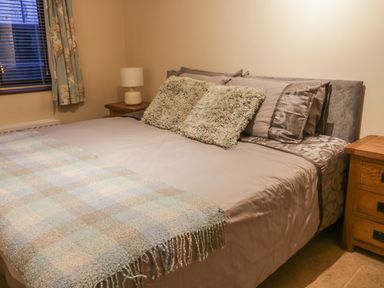 A bedroom with a bed with pillows and a throw blanket two bedside tables with lamps and a window with curtains at Hill Bank in Hutton Roof