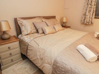 A bedroom with a bed with beige bedding pillows and towels on it and two bedside tables with lamps at Hill Bank in Hutton Roof