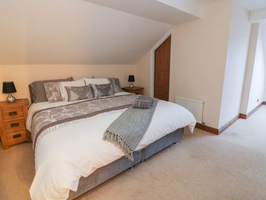 A bedroom with a bed with pillows and a blanket two wooden nightstands with lamps and a closed wooden door at Hill Bank in Hutton Roof