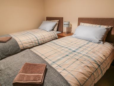 A bedroom with two single beds with checkered bedding and folded towels on gray blankets at Hill Bank in Hutton Roof