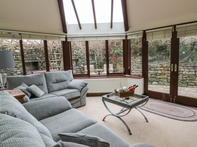 A room with two grey sofas a glass coffee table and large windows overlooking a stone wall at Hill Bank in Hutton Roof
