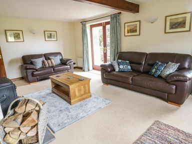 A living room with two leather sofas a wooden coffee table and firewood at Hill Bank in Hutton Roof