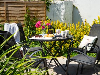 A garden patio with black chairs around a glass table with coffee mugs croissants and flowers at 3 Horse Pool Road in Laugharne
