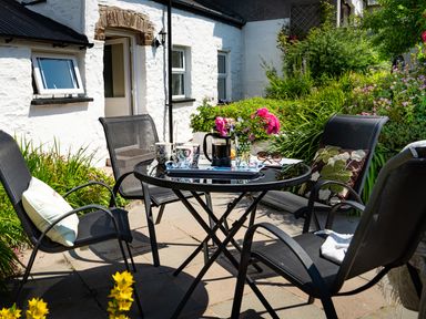 An outdoor patio area with a glass table and four black chairs surrounded by greenery at 3 Horse Pool Road in Laugharne