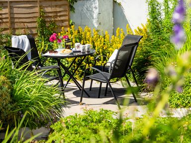 A garden patio with a round table and three chairs surrounded by plants and flowers at 3 Horse Pool Road in Laugharne