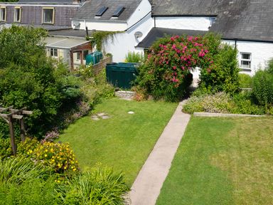 A garden with grass, flower beds, a pathway, and a white building with a floral arch at 3 Horse Pool Road in Laugharne