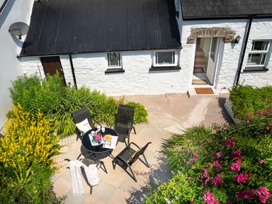 A patio with a glass table and four black chairs surrounded by plants at 3 Horse Pool Road in Laugharne