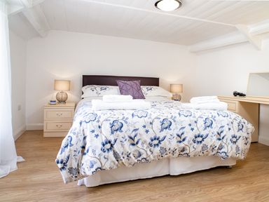 A bedroom with a double bed covered with a floral bedspread two bedside tables with lamps and a dressing table with a mirror and hairdryer at 3 Horse Pool Road in Laugharne