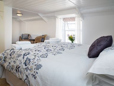 A bedroom with a bed with floral bedding towels on the bed wicker chairs and a window with flowers at 3 Horse Pool Road in Laugharne