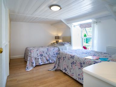 A bedroom with two single beds with floral bedspreads a window with curtains and a bedside table with a lamp at 3 Horse Pool Road in Laugharne
