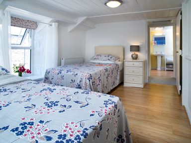 A bedroom with two single beds floral bedspreads nightstand with lamp window and bathroom doorway at 3 Horse Pool Road in Laugharne