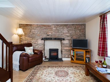 A living room with a leather armchair stone fireplace TV on wooden stand and a wooden coffee table with wine glasses at 3 Horse Pool Road in Laugharne