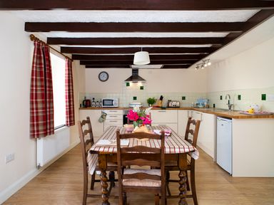 A kitchen with wooden table and chairs a checked tablecloth and red plaid curtains at 3 Horse Pool Road in Laugharne