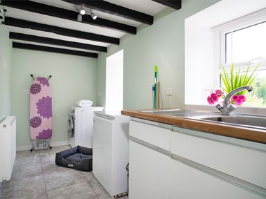 A laundry room with a washing machine, ironing board, mop, sink, and pet bed at 3 Horse Pool Road in Laugharne