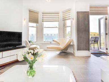 A living room with white chairs a television and flowers on a table at No 6 Arlington Villas in Ilfracombe