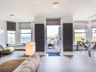 A living room with beige sofa chairs dining table with chairs and a balcony overlooking the sea at No 6 Arlington Villas in Ilfracombe