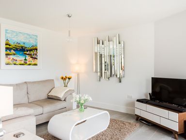 A living room with a beige sofa a white modern coffee table a flat screen TV on a wooden and white cabinet a floor lamp and decorative wall mirror at No 6 Arlington Villas in Ilfracombe