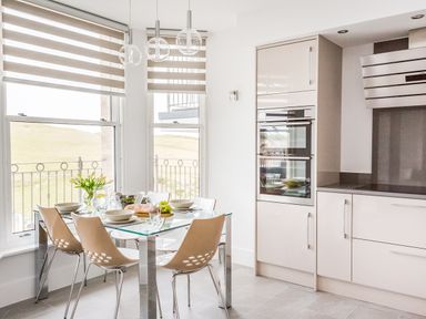 A kitchen with a glass dining table set for six near windows with blinds at No 6 Arlington Villas in Ilfracombe