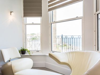 A seating area with modern chairs near large windows overlooking a balcony with railings and a sea view at No 6 Arlington Villas Ilfracombe