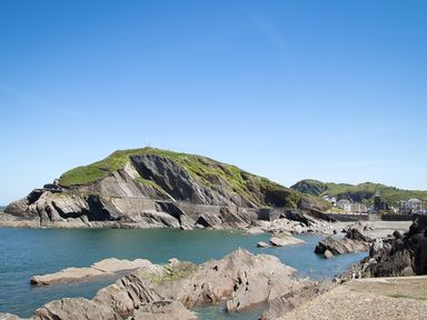 A coastal landscape with rocky cliffs green hills and buildings in the distance at No 6 Arlington Villas in Ilfracombe