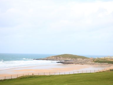 A coastal scene with a sandy beach rolling waves a green grassy area and houses on rocky cliffs at Little Fistral in Fistral