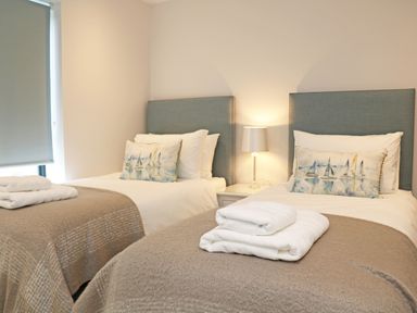 A bedroom with two single beds blue headboards bedside table with lamp and folded towels on beds at Little Fistral in Fistral