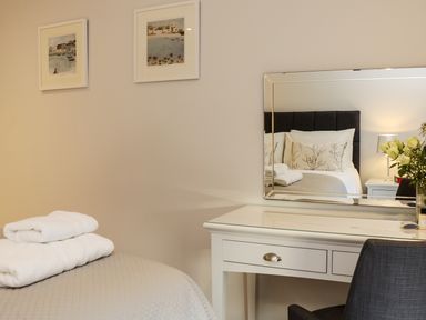 A bedroom with a bed reflected in a mirror above a white desk with a chair and folded towels on the bed at Little Fistral in Fistral