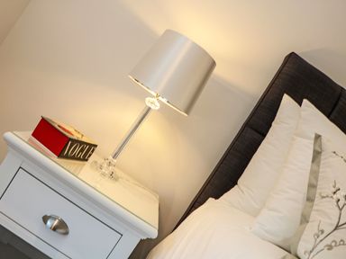 A bedside table with a lamp and a book next to a bed with pillows and a dark headboard at Little Fistral in Fistral