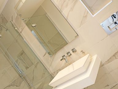 A bathroom with a wall-mounted sink a large mirror and a glass shower enclosure at Little Fistral in Fistral