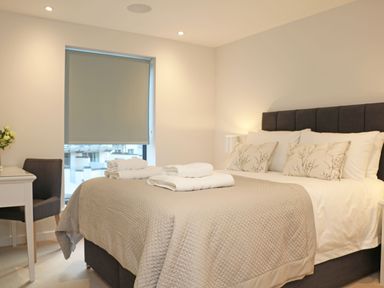 A bedroom with a bed covered in a beige quilt and white towels on top with a window and desk with chair at Little Fistral in Fistral