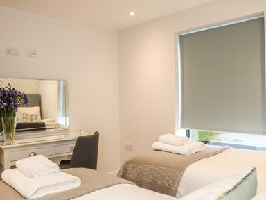 A bedroom with two beds with towels on them a desk with a mirror and flowers and a window with a blind at Little Fistral in Fistral