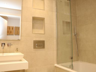 A bathroom with a white sink faucet recessed shelves a bathtub with a glass shower screen and a handheld shower at Little Fistral in Fistral