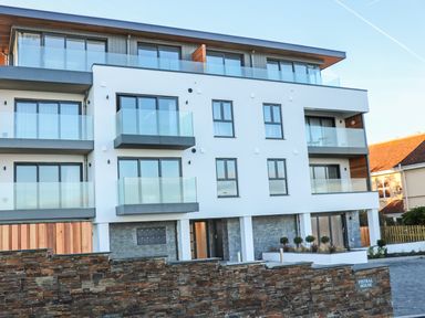 The exterior of a modern three-story building with glass balconies and a stone wall in front at Little Fistral in Fistral