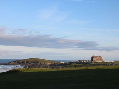 A coastline with grassy land and a large building near the shore at Little Fistral in Fistral