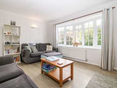 A living room with grey sofas a wooden coffee table a white bookshelf and a large window with curtains at Glan Dwr in Red Wharf Bay