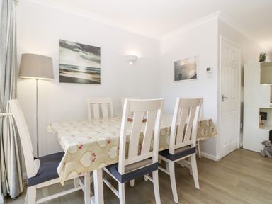 A dining room with a table covered by a patterned tablecloth and white chairs at Glan Dwr in Red Wharf Bay