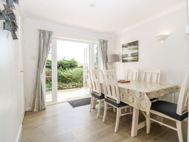 A dining room with a table and six chairs near open glass doors leading to a garden at Glan Dwr in Red Wharf Bay