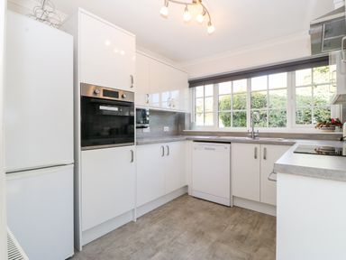 A kitchen with white cabinets appliances and a large window at Glan Dwr in Red Wharf Bay