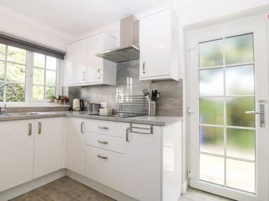 A kitchen with white cabinets a countertop a stovetop a sink near a window and a glass door at Glan Dwr in Red Wharf Bay