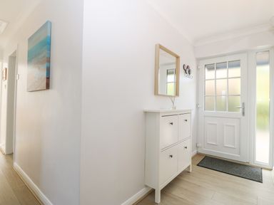 An entryway with a white front door a white shoe cabinet a mirror above it and a painting on the wall at Glan Dwr in Red Wharf Bay