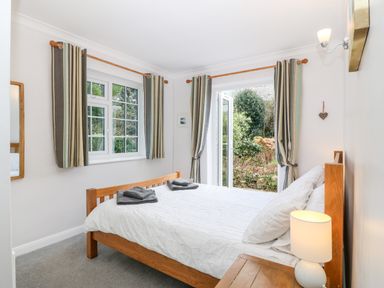 A bedroom with a wooden bed and white bedding next to a window and glass door with curtains at Glan Dwr in Red Wharf Bay
