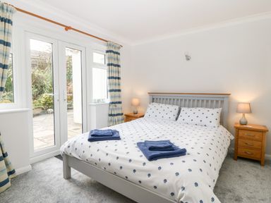 A bedroom with a double bed with polka dot bedding and blue towels two bedside tables with lamps and glass doors with curtains at Glan Dwr in Red Wharf Bay
