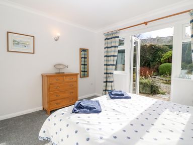 A bedroom with a bed towel sets on it a wooden dresser a wall mirror and open double doors leading outside at Glan Dwr in Red Wharf Bay